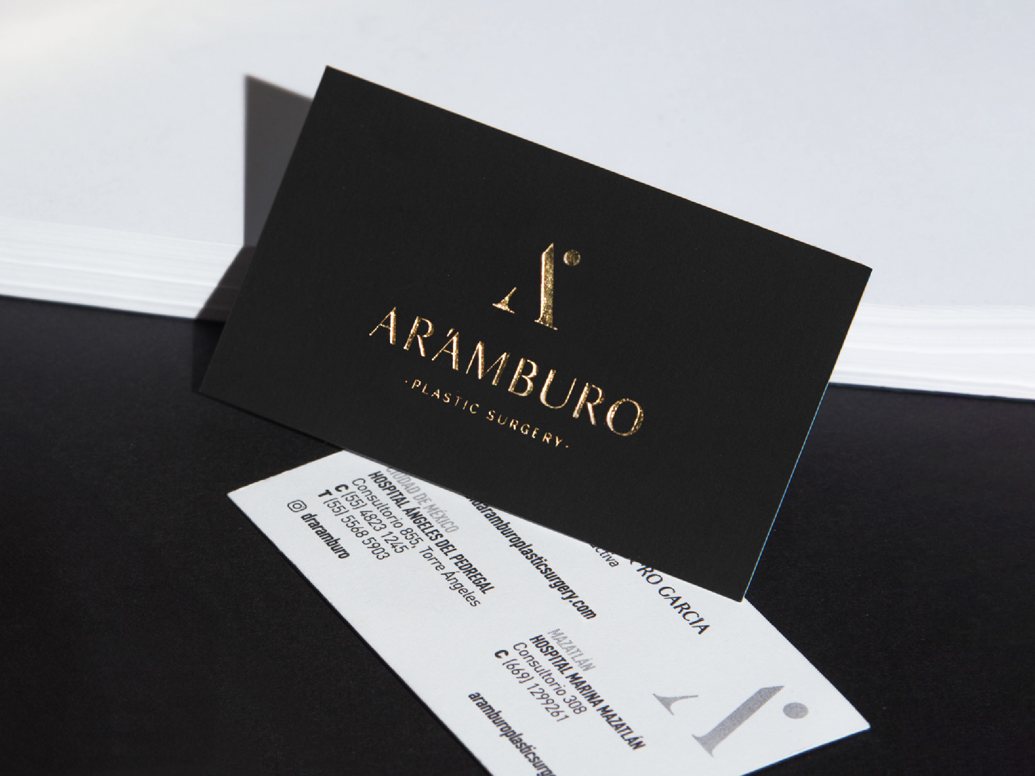 Tarjetas de presentación negras con hot stamping dorado de Arámburo Plastic Surgery, diseño gráfico premium para marca médica estética.